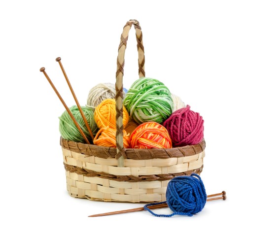 A basket of yarn in the colors of green, yellow, orange, mauve and blue with knitting needles