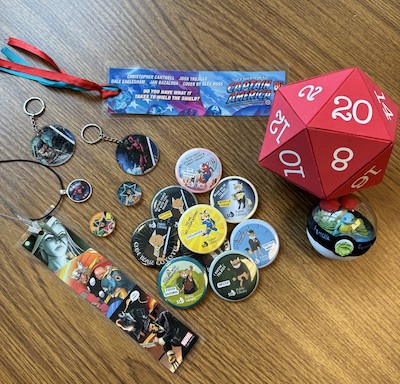 Display of comic con makes including: comic-themed bookmarks, magnets, pendants, and keychains plus pokeball terrarium and giant foam D20 die