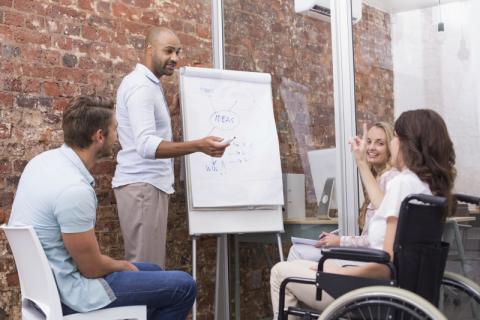 3 people sitting in a circle around a man with a large display pad.