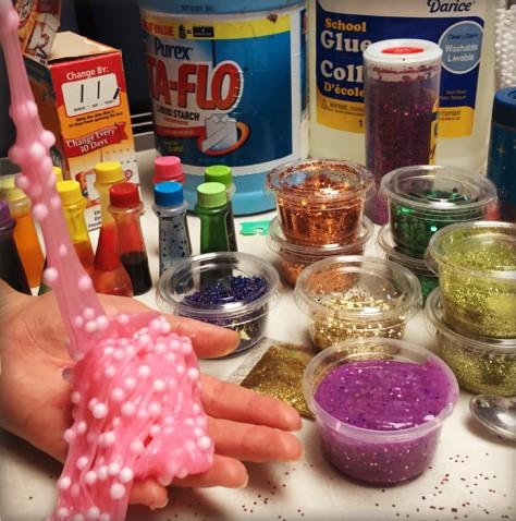 Hand holding pink slime in front of various slime ingredients