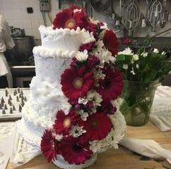 tiered cake with white frosting, decorated with red flowers