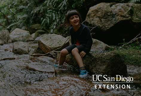 YOUNG PERSON SITTING ON A ROCK IN A CREEK