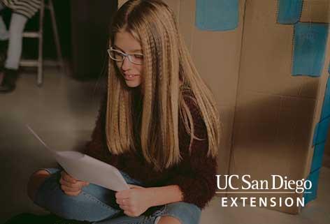 Girl sitting on the floor of a classroom, reading from a document