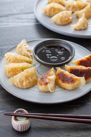 Gyoza arranged on a plate with dipping sauce and chopsticks.