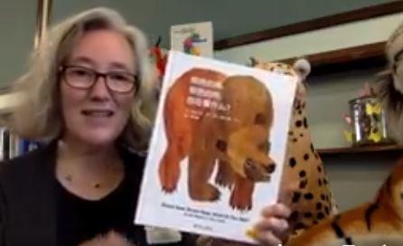 Miss Kristen showing the cover of a copy of the book, "Brown Bear, Brown Bear, What Do You See?"