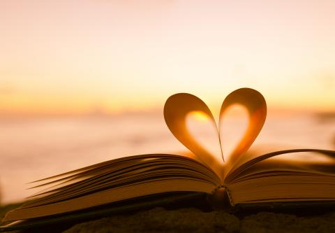 Photograph of an open book, its pages making a heart shape, in front of a beach background