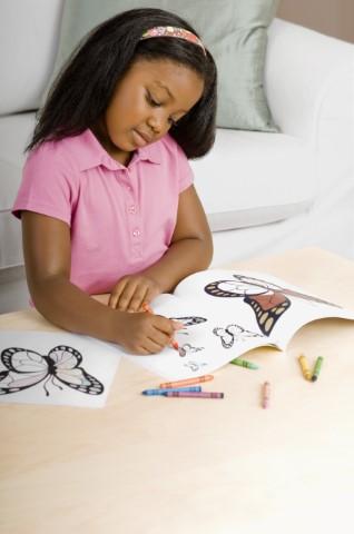 A girl coloring a butterfly in a coloring book.