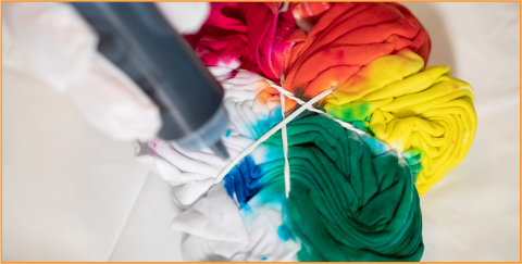 White t-shirt tied up and being dyed with primary colors of red, orange, yellow, green, and blue