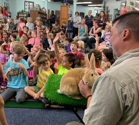 Man holds bunny in front a audience of children.