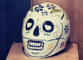 Photograph of a motorcycle helmet painted to look like a Día De Los Muertos sugar skull by artist Erica Alarcon. 