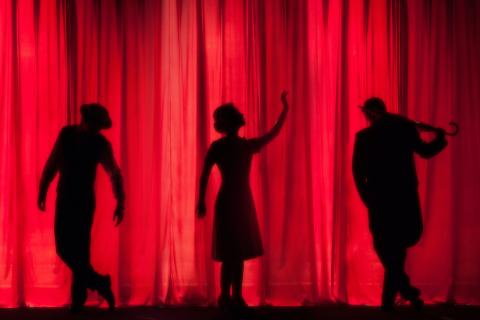 3 actors in silhouette stand in front of a red curtain 