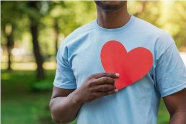 A man holds up a red paper heart up to his chest.