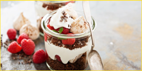A small glass jar with whipped cream, raspberries and chocolate.