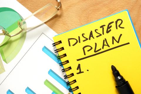 Photo of a tabletop with a notebook and pen and other materials related to formulating a disaster plan
