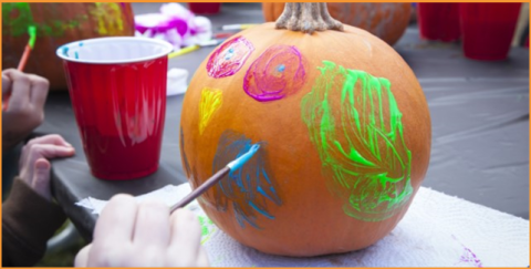 A child's hand painting a pumpkin