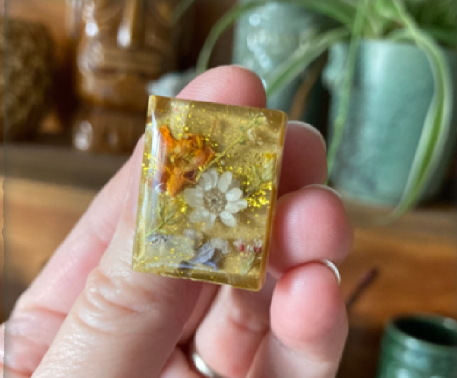 Hand holding a rectangular piece of resin jewelry with a flower design
