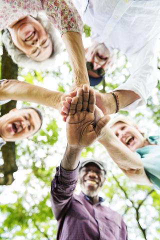 Photo from below of a group of seniors standing in a circle in putting their hands in the middle