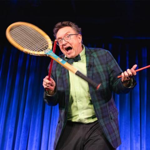 Smiling man juggling a tennis racket with a percussion stick