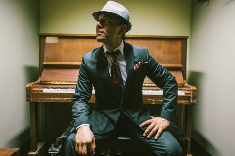 Irving Flores sitting in front of an upright piano