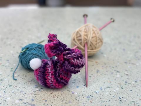Photo of a knitted rabbit, next to balls of yarn with a crochet hook and knitting needles