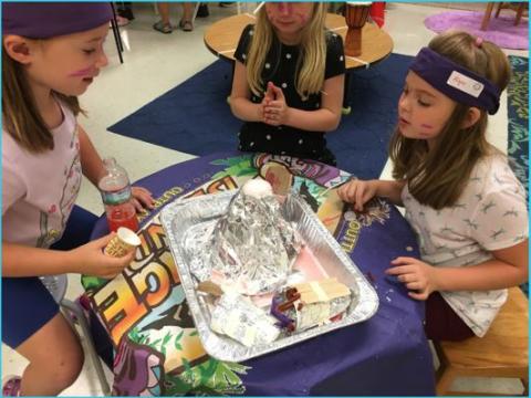 Group of three girls watching a tin foil volcano model erupt