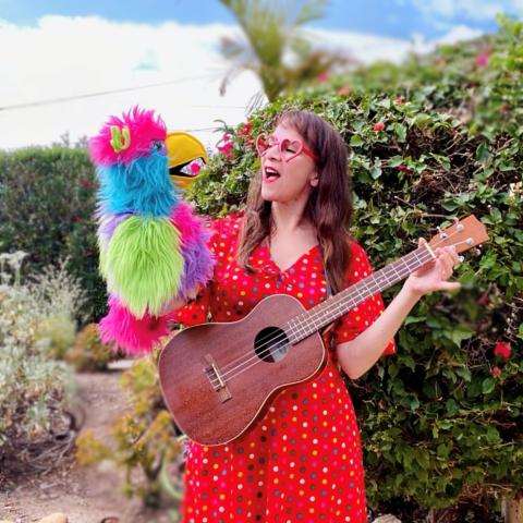 Hooray Miss Marae holding a multi-colored parrot puppet and a ukelele