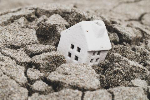 Tiny white model house in big pothole