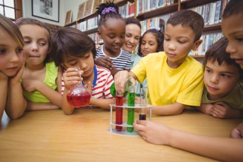 A group of young children pouring different colored liquids from flasks into test tubes.
