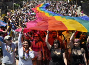Photograph of the San Diego Pride Parade featuring a street full of people holding up an extremely long rainbow flag.