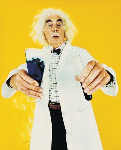 Man in a lab coat holding a chemistry beaker and test tube with a yellow background