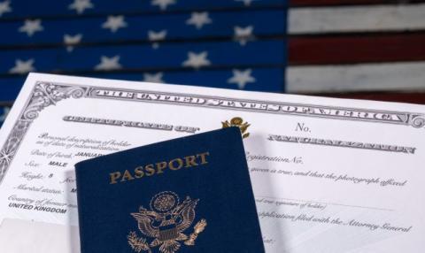 US Passport on top of a Certificate of Naturalization with the US flag in the background.