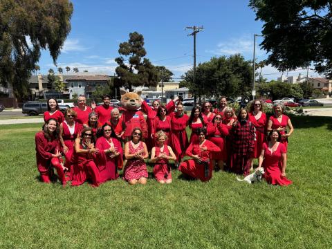 Many people (and a coyote) in red dresses, sitting together in a park.  