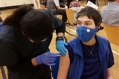 A nurse administering a shot in the upper arm of a masked person.  