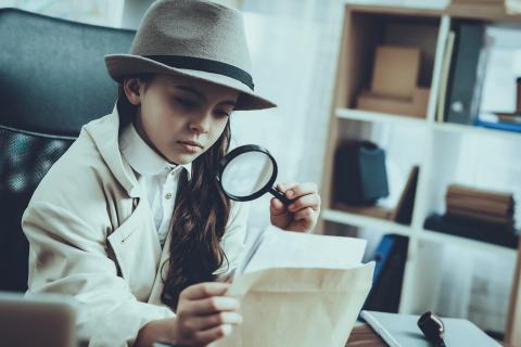 Girl detective examining a sheet of paper with a magnifying glass.