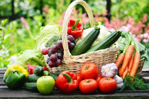 woven basket on an outdoor table filled with vegetables and with vegetables next to the basket