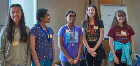5 girls, around the ages of 10-13, standing at the front of a room and smiling.