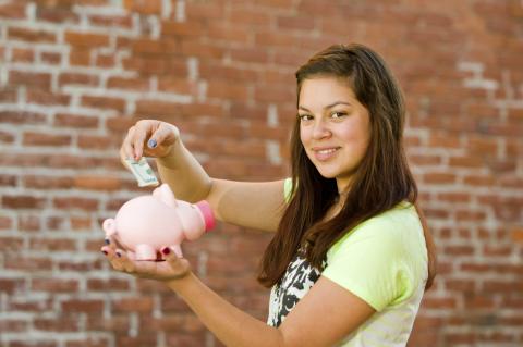 woman with long hair holding a pink piggy bank and putting money into it
