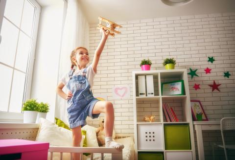 Girl, around age 6, pretending to fly a toy airplane in her bedroom.