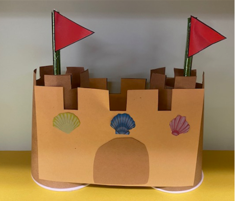 A sandcastle made out of paper cups, colored paper, stickers, and straws