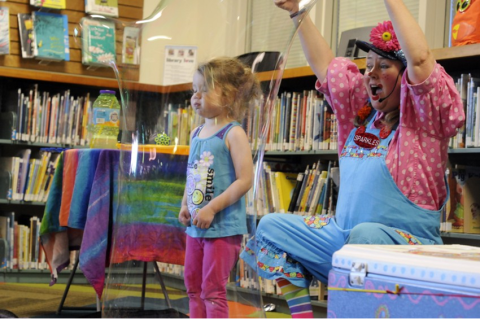 Sparkles the Clown creating a giant bubble over a little girl