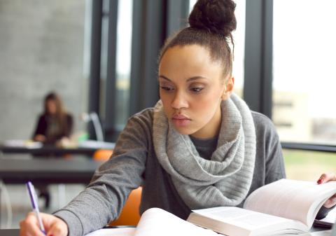 Woman taking notes with an open book in front of her