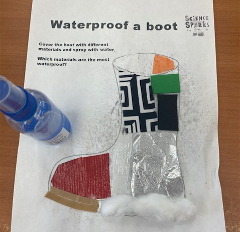 A spray bottle next to a paper boot covered in tin foil, cotton, felt, tissue paper, and other materials