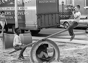 Black and white photograph of children playing on a seesaw.