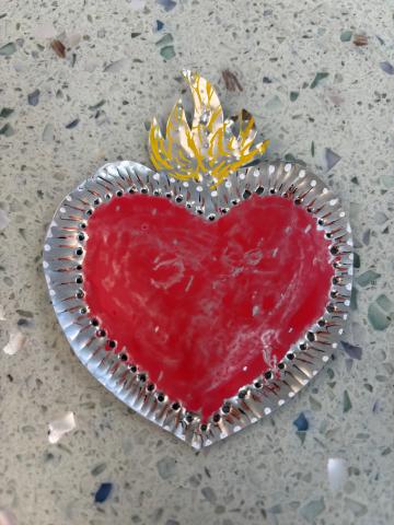 A heart made from a piece of metal, with painted areas and small holes punched around the edges.