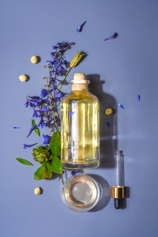 Photo of a glass bottle with a dropper, surrounded by flowers and herbs