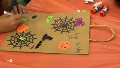 A child coloring a trick or treat bag that is decorated with stickers and paper spiderwebs