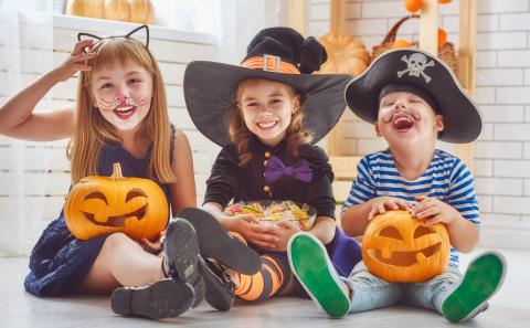 Three children sit in costumes with jack-o-lanterns