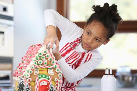 girl decorating a gingerbread house with candy and icing