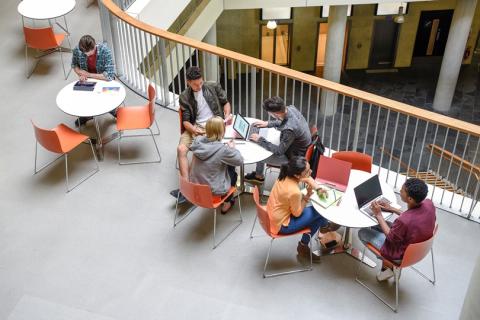 multiple groups of college students working at small round tables on a balcony