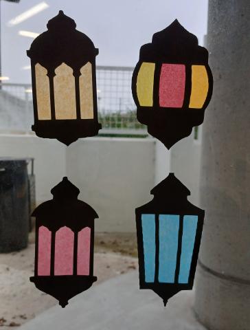 Four paper lanterns hanging in a window so light shines through the tissue paper.